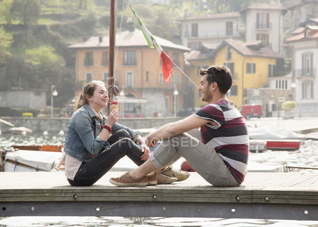 Couple sitting on pier eating ice cream cone at lake Mergozzo, Verbania, Piemonte, Italy — Stock Photo