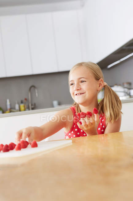 Chica sonriente poniendo frambuesas en los dedos - foto de stock