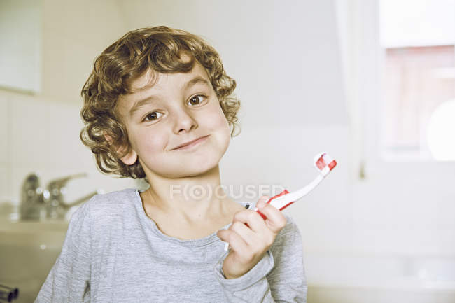 Портрет хлопчик у ванній кімнаті проведення зубна щітка, дивлячись на камеру посміхається — стокове фото