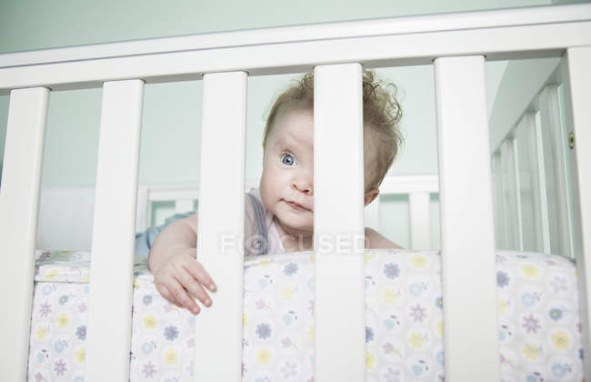 Porträt eines kleinen Mädchens, das durch Gitterstäbe auf dem Kinderbett blickt — Stockfoto