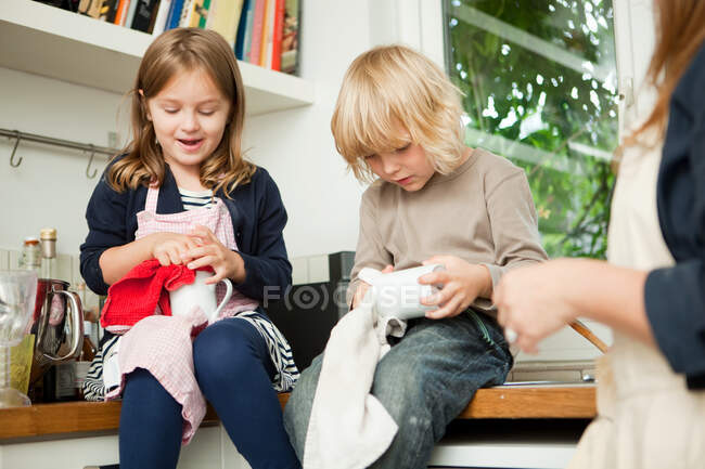 Siblings drying cups on kitchen counter — Stock Photo