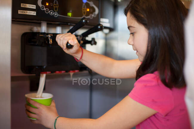 Fille versant tasse de yaourt glacé — Photo de stock