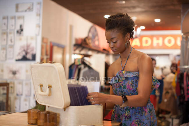 Giovane donna che guarda attraverso la scatola di oggetti nel negozio vintage — Foto stock