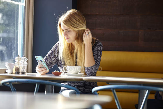Young woman alone in cafe reading smartphone texts — Stock Photo