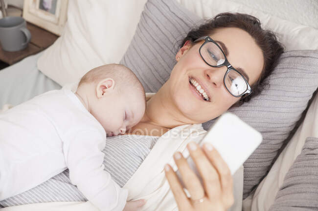 Bambino che dorme sulla madre, madre usando lo smartphone — Foto stock