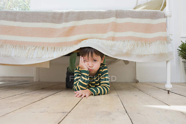 Menino escondido debaixo de uma cama — Fotografia de Stock