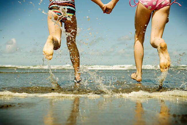Two girls holding hands running into sea — Stock Photo