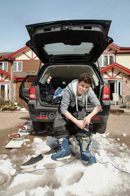 Young man sitting on car boot tying snow boot laces — Stock Photo