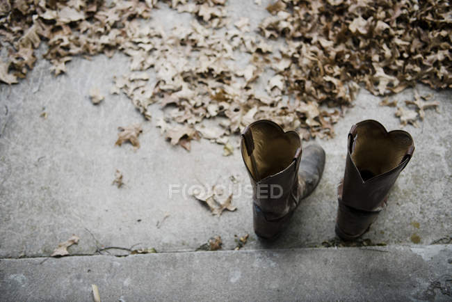Par de botas de vaquero sobre asfalto con hojas caídas - foto de stock