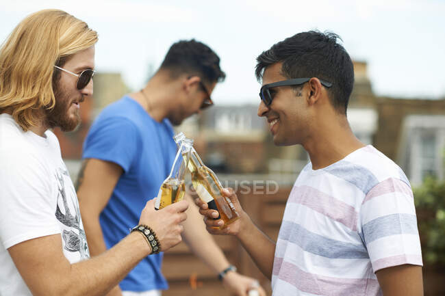 Due amici maschi fanno un brindisi con birra in bottiglia alla festa sul tetto — Foto stock