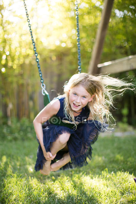 Ritratto di ragazza accovacciata mentre oscilla sull'altalena del giardino — Foto stock