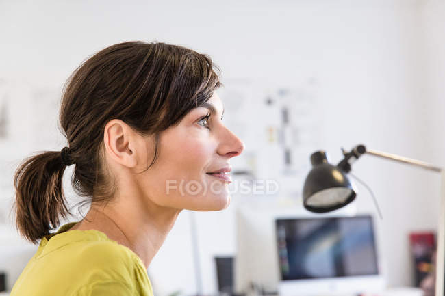 Вид збоку зрілої жінки в офісі дивиться в очі посміхаючись — стокове фото