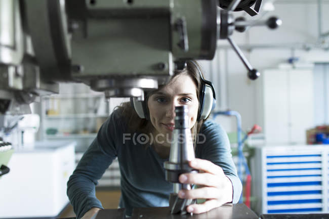 Mujer en el taller con defensores del oído operando máquina sonriendo - foto de stock
