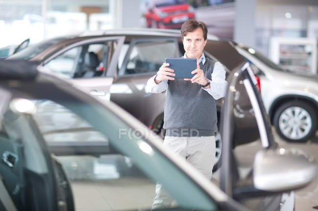 Мужчина фотографирует автомобиль с цифровым планшетом в выставочном зале — стоковое фото