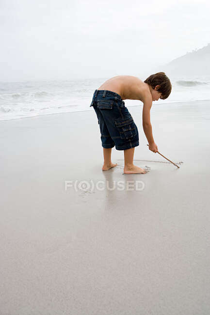 Мальчик рисует на песке — стоковое фото
