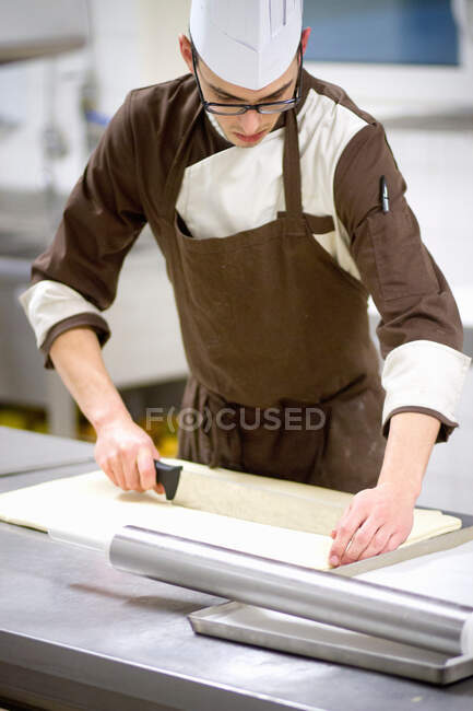 Baker slicing dough in kitchen — Stock Photo