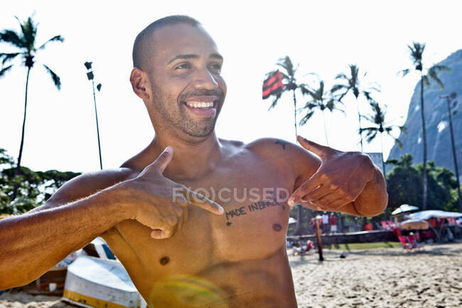 Man on beach pointing to chest with tattoo saying Made In Brazil — Stock Photo