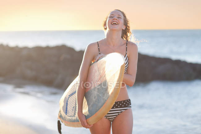 Young woman carrying surfboard on beach — Stock Photo