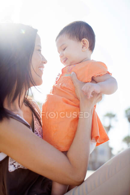 Mitte erwachsene Frau hält Tochter im Sonnenlicht und lächelt — Stockfoto