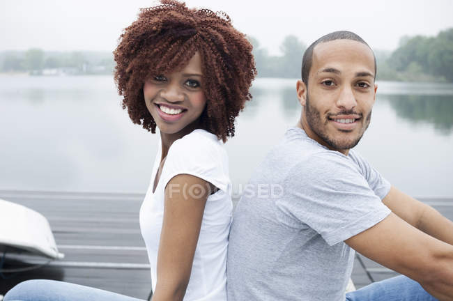 Портрет молодой пары, улыбающейся спиной к спине — стоковое фото