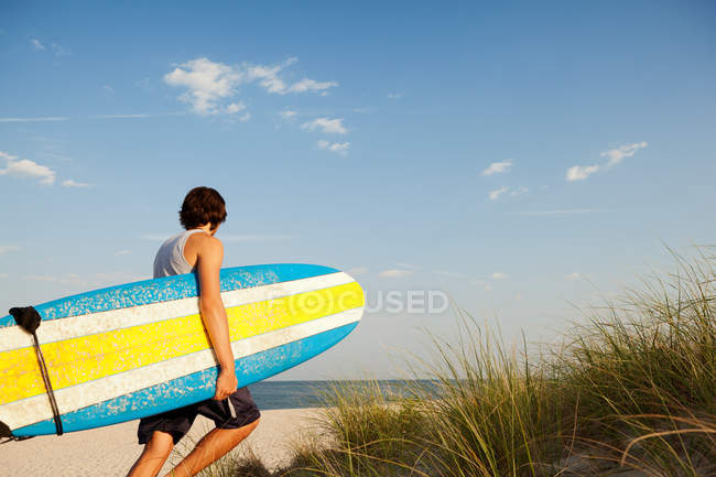 Teenager carrying surfboards to beach beside dunes — Stock Photo