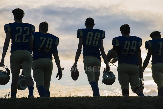 Group of young american football players walking away, rear view — Stock Photo