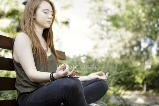 Jeune femme pratiquant position de yoga lotus sur banc de parc — Photo de stock