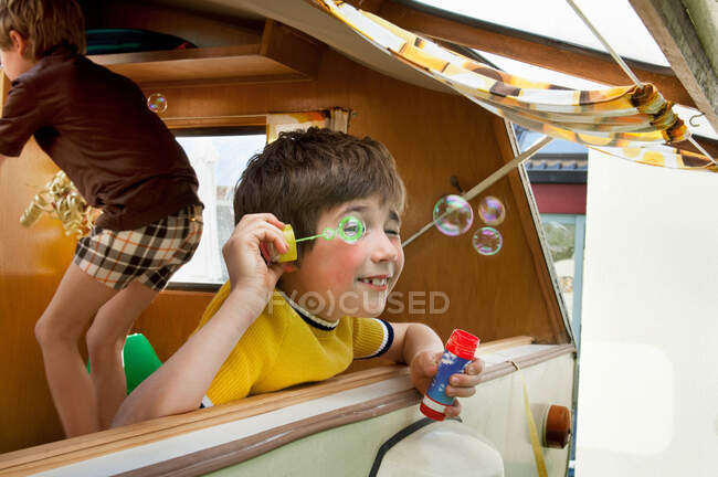 Two boys blowing bubbles out of caravan — Stock Photo
