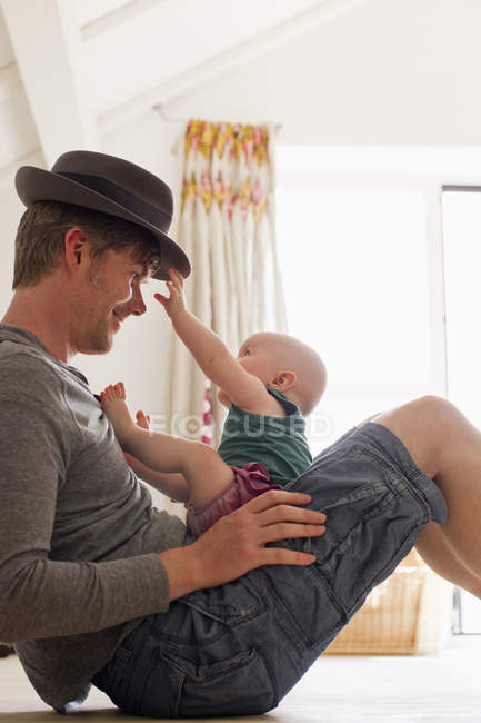 Padre con sombrero sosteniendo a la niña en el regazo - foto de stock