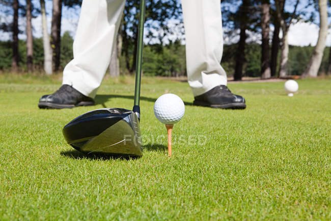 Golf player feet and ball with golf club on foreground — Stock Photo