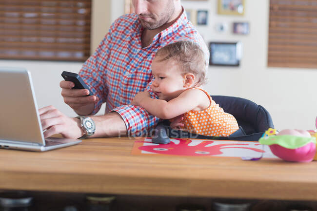 Man working at kitchen counter with baby sitting beside — Stock Photo