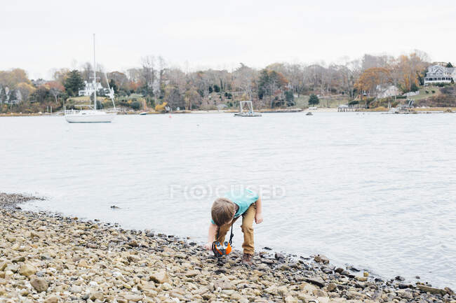Giovane ragazzo raccogliendo pietre accanto lago — Foto stock