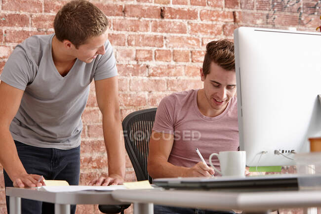 Jóvenes hablando en el escritorio con computadora - foto de stock