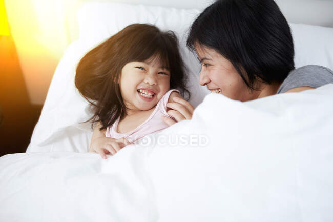 Young Chinese mother and daughter laying in bed together at home — Stock Photo