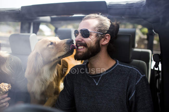 Собака облизує молодого чоловіка бородатим обличчям в джипі — стокове фото