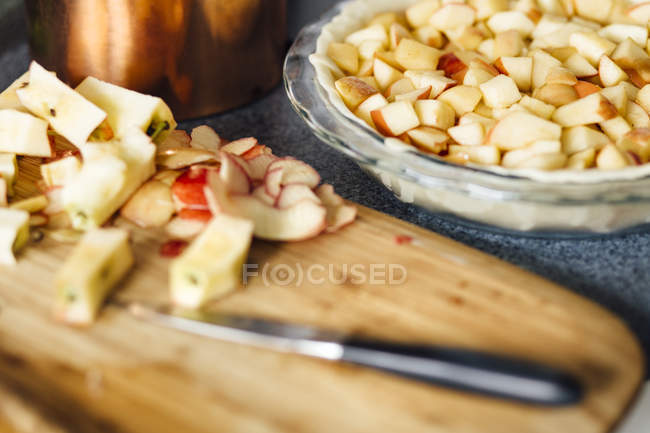 Chopped apples in raw pastry and on wooden board with knife — Stock Photo