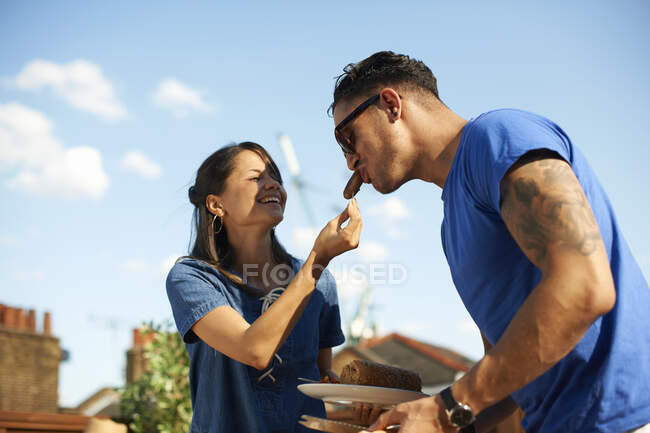 Mid adult woman feeding sausage to boyfriend at rooftop party — Stock Photo