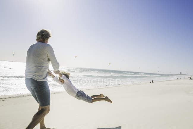 Отец размахивает сыном на пляже — стоковое фото