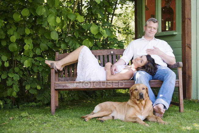 Retrato de casal maduro no banco de jardim com cão — Fotografia de Stock