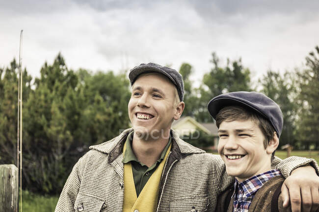 Homme portant une casquette plate, bras autour du garçon regardant loin en souriant — Photo de stock