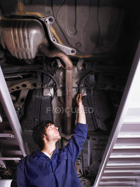 Механик, стоящий под поднятым автомобилем — стоковое фото