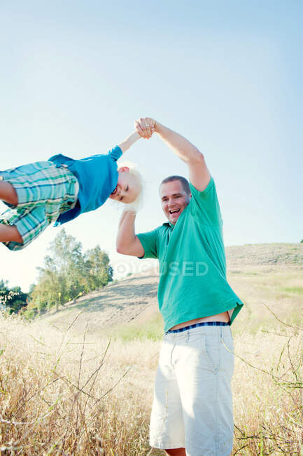 Hombre balanceo hijo en el campo - foto de stock