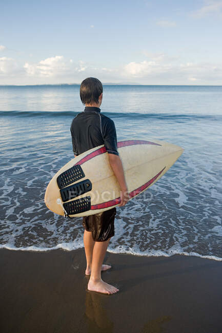 Auckland, joven con tabla de surf en la playa de Muriwai - foto de stock