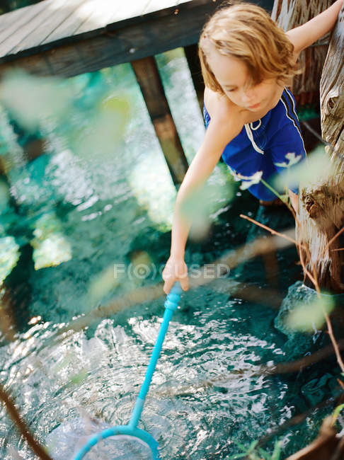 Young boy leaning over pond with fishing net — Stock Photo