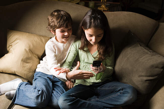Un hermano y una hermana usando un teléfono celular - foto de stock