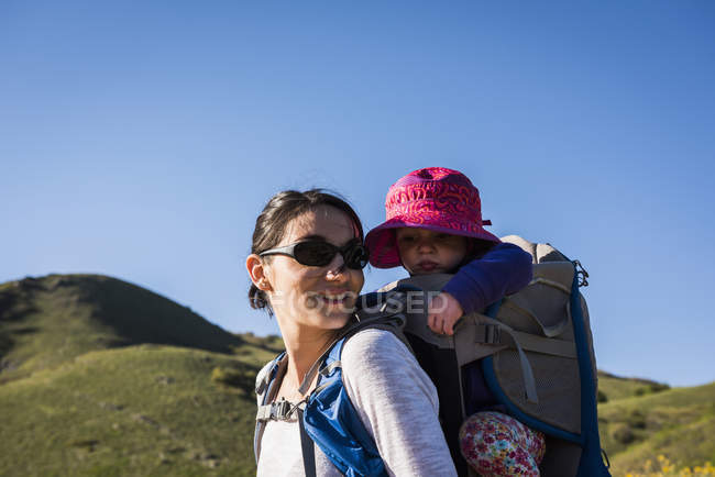 Mother carrying young daughter on back, hiking the Bonneville Shoreline Trail in the Wasatch Foothills above Salt Lake City, Utah, USA — Stock Photo
