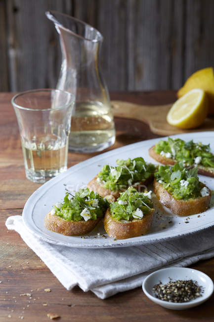 Still life of bruschetta with peas, goats cheese, salt and pepper — Stock Photo