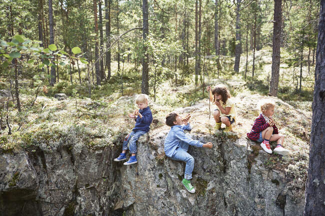 Children sitting on rocks in forest eating picnic — Stock Photo