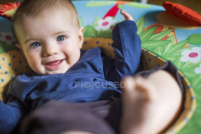 Niña en asiento de bebé mirando a la cámara sonriendo - foto de stock