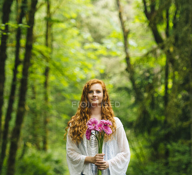 Young woman holding bunch of pink gerberas in forest — Stock Photo